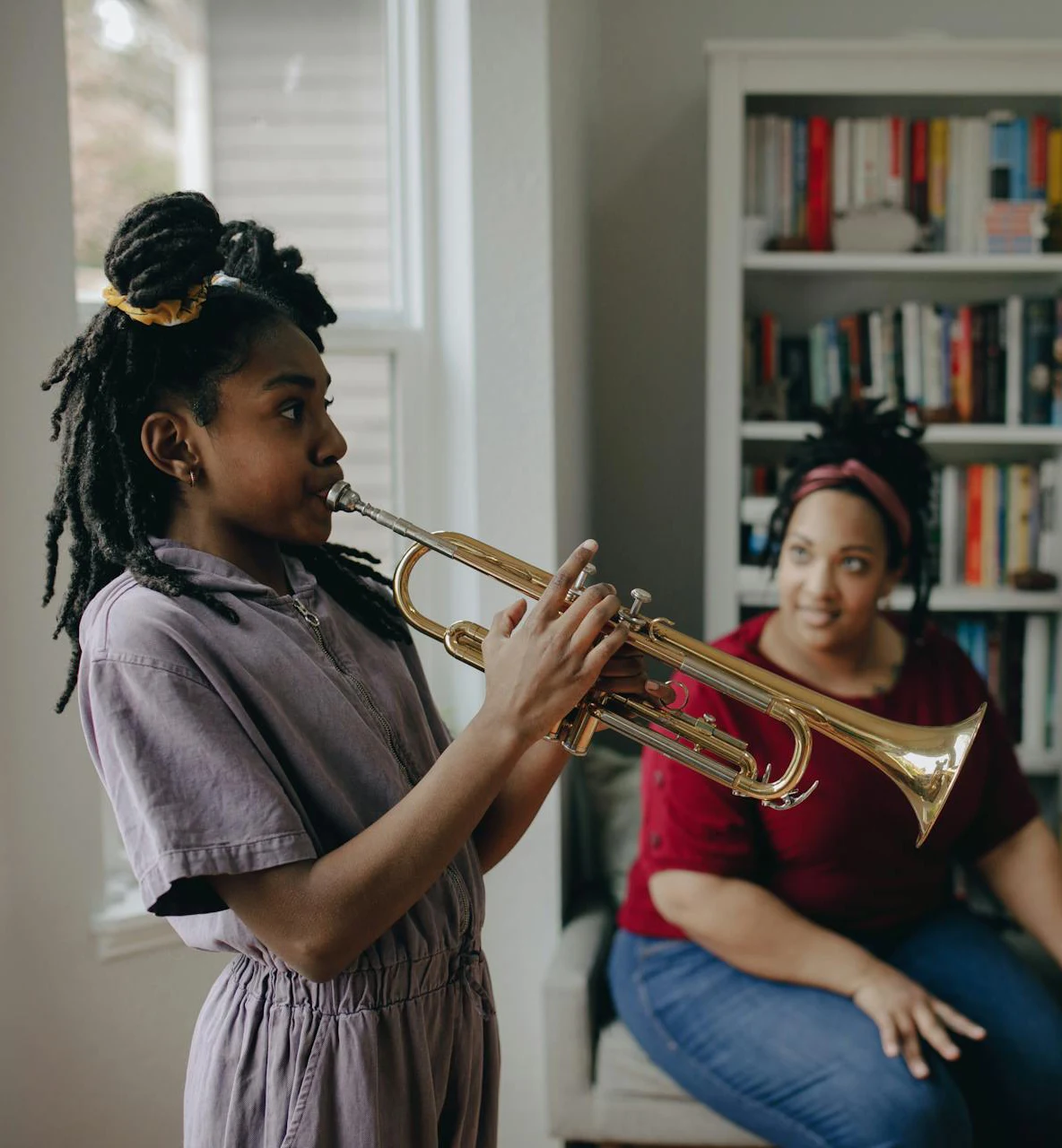 A girl is playing trumpet in her living room in Atlanta and her teacher is observing her