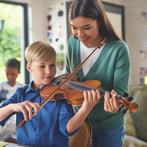 A 10 year old child from Atlanta is playing a violin in his house while his violin teacher from Imagine Arts school is helping him