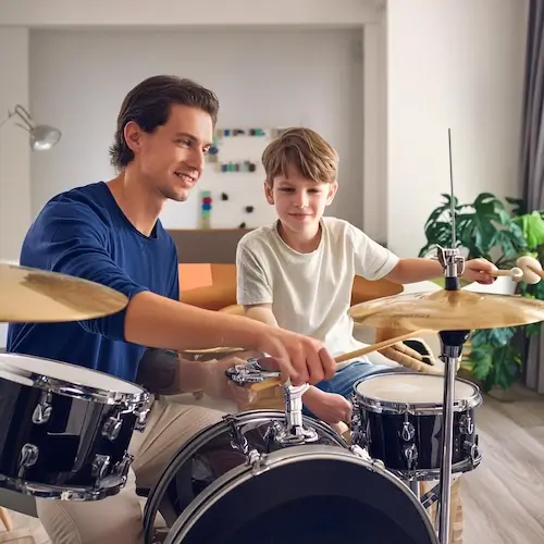 A 12 year old child from Atlanta is playing drums in his house while his drum teacher from Imagine Arts school is helping him
