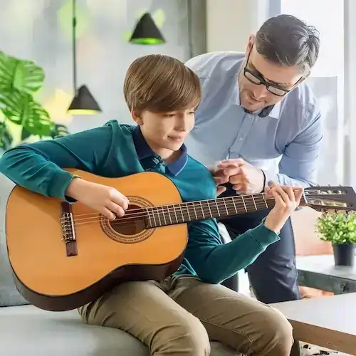 A 15 year old child from Atlanta is playing a guitar in his house while his guitar teacher from Imagine Arts school is helping him 1 1 1 2